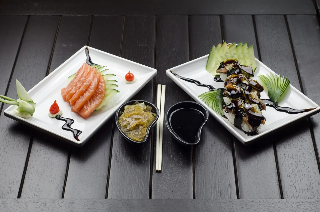 Salmon sashimi and an eel roll plated on white dishes with soy sauce